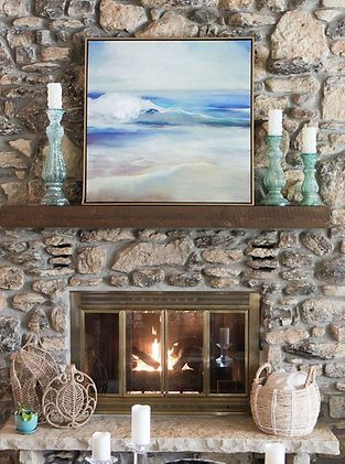 A stone fireplace with a painting above it and candles on the mantle.