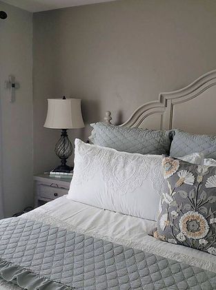 A bedroom with a bed , nightstand , lamp and pillows.