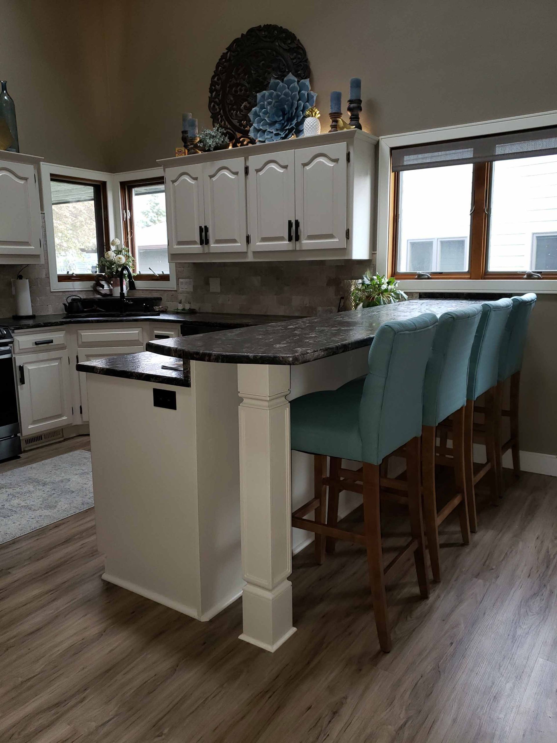 A kitchen with white cabinets , granite counter tops , and blue chairs.