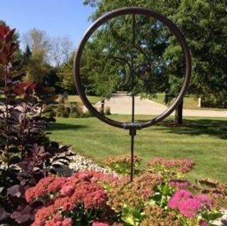 A circular sculpture is sitting in the middle of a garden surrounded by flowers.