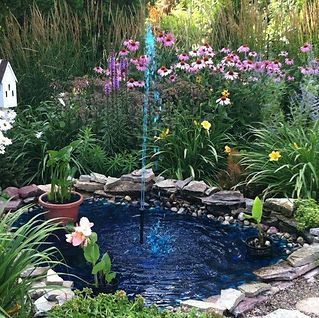 There is a fountain in the middle of the garden surrounded by flowers.