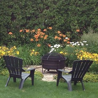 Two chairs sit in front of a fire pit in a garden