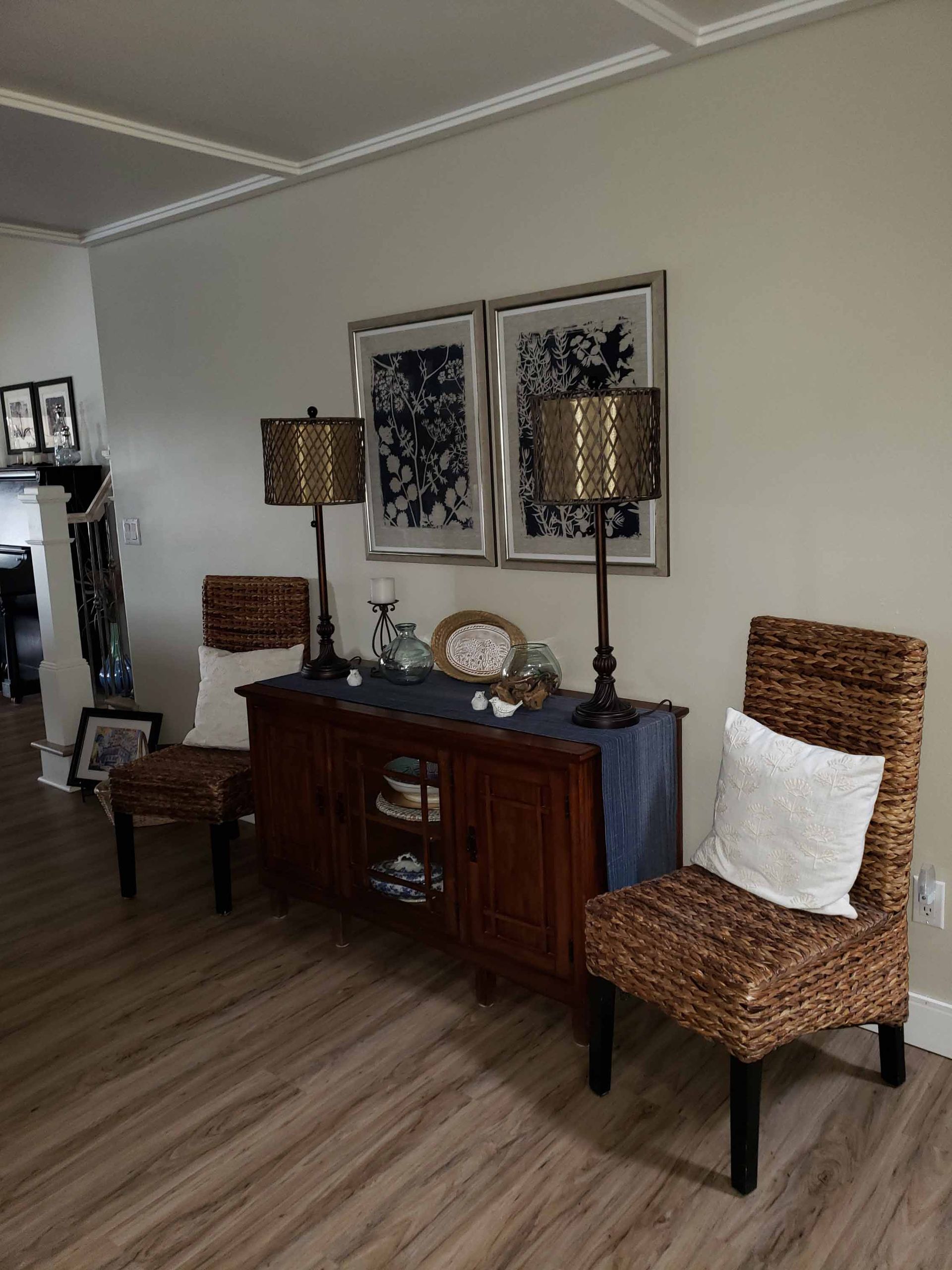 A living room with two chairs , a dresser , two lamps and two pictures on the wall.