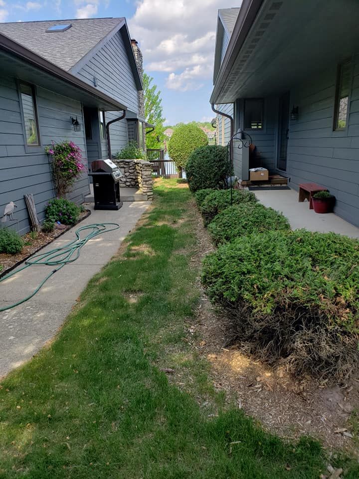 A narrow walkway between two houses with a grill and a hose.