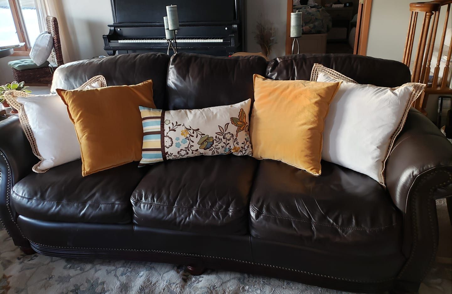 A brown leather couch with many pillows on it in a living room.