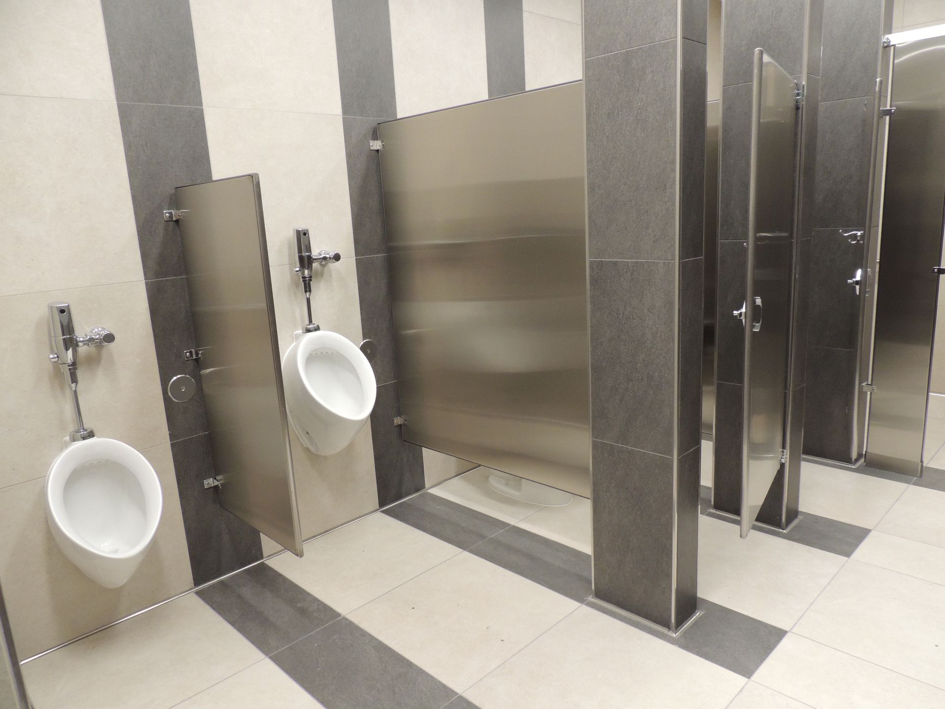 A public restroom with urinals and stainless steel partitions