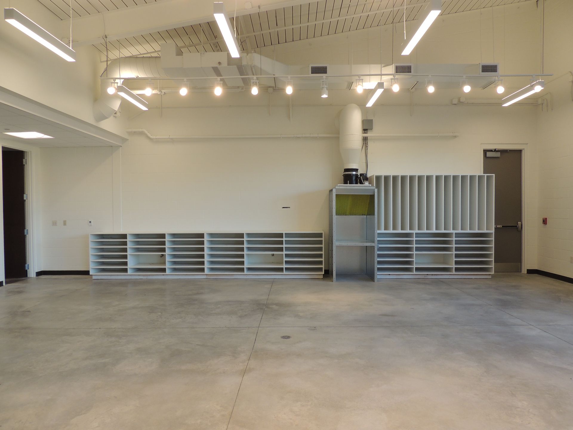 A large empty room with a lot of shelves and lights hanging from the ceiling.