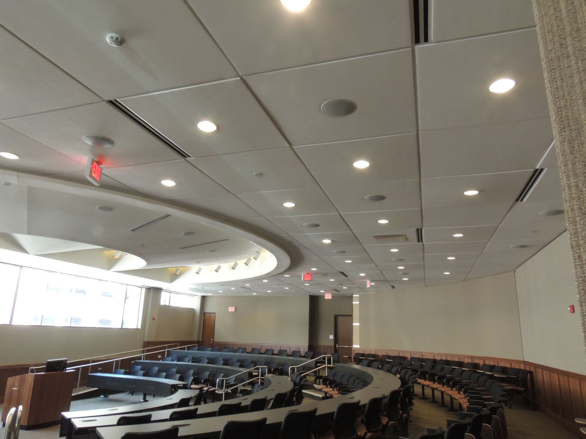 A large auditorium with tables and chairs and a red exit sign