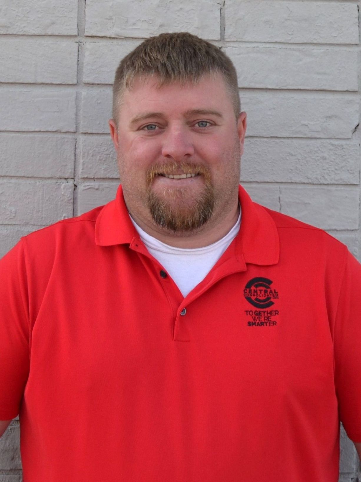 A man with a beard is wearing a red Central Consolidated shirt.