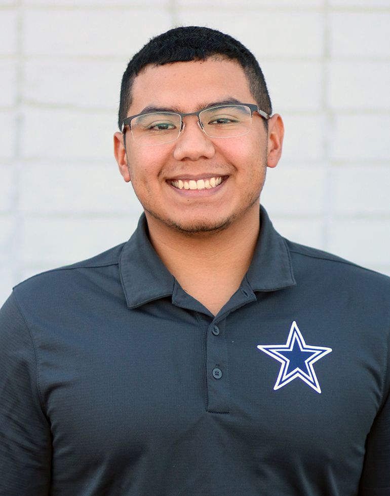 A young man wearing glasses and a polo shirt with a star on it is smiling.