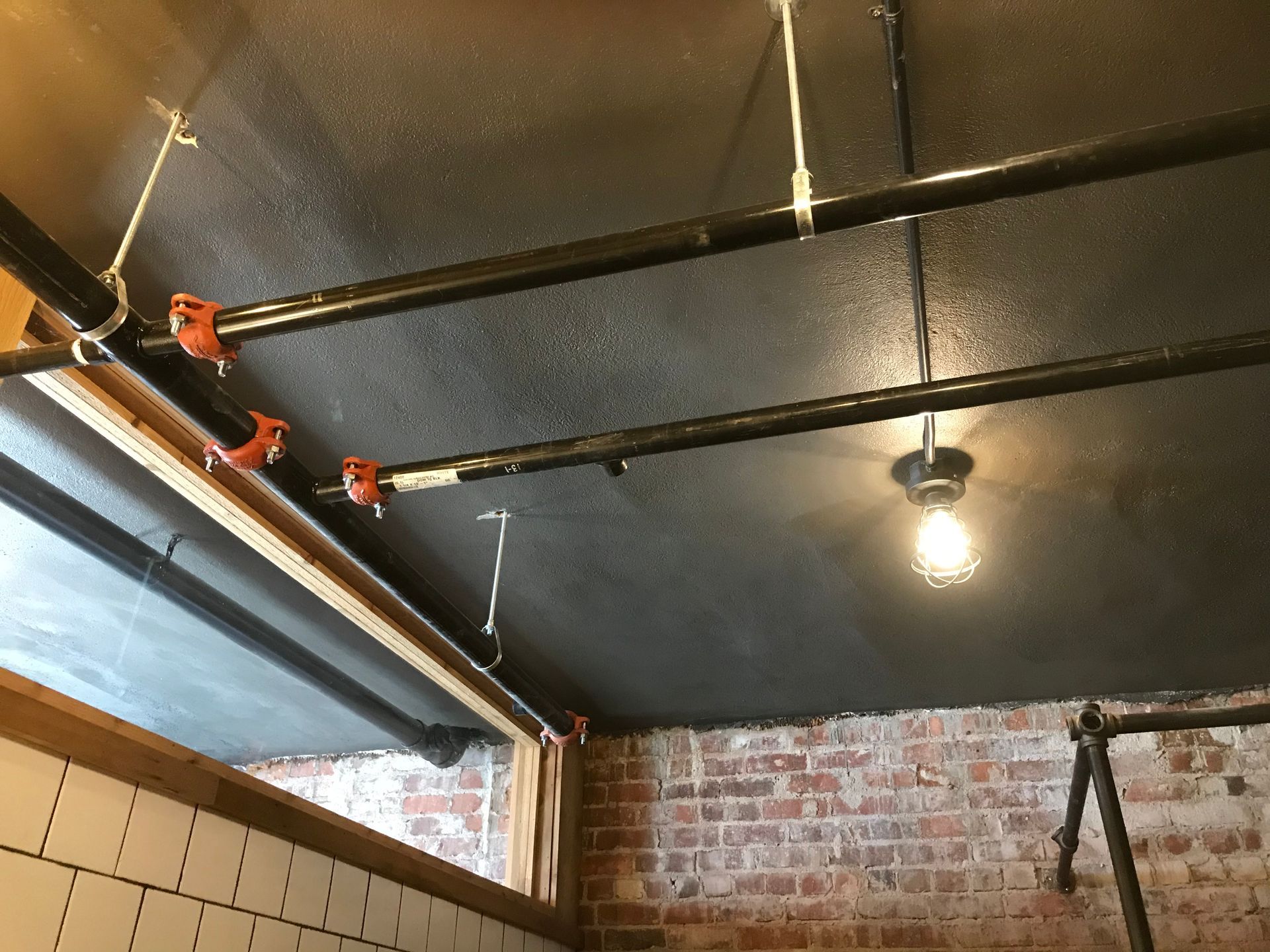 A ceiling with pipes and a light hanging from it