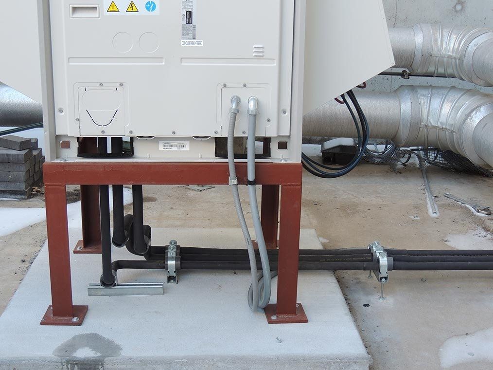 A white box is sitting on top of a concrete platform surrounded by pipes and wires.