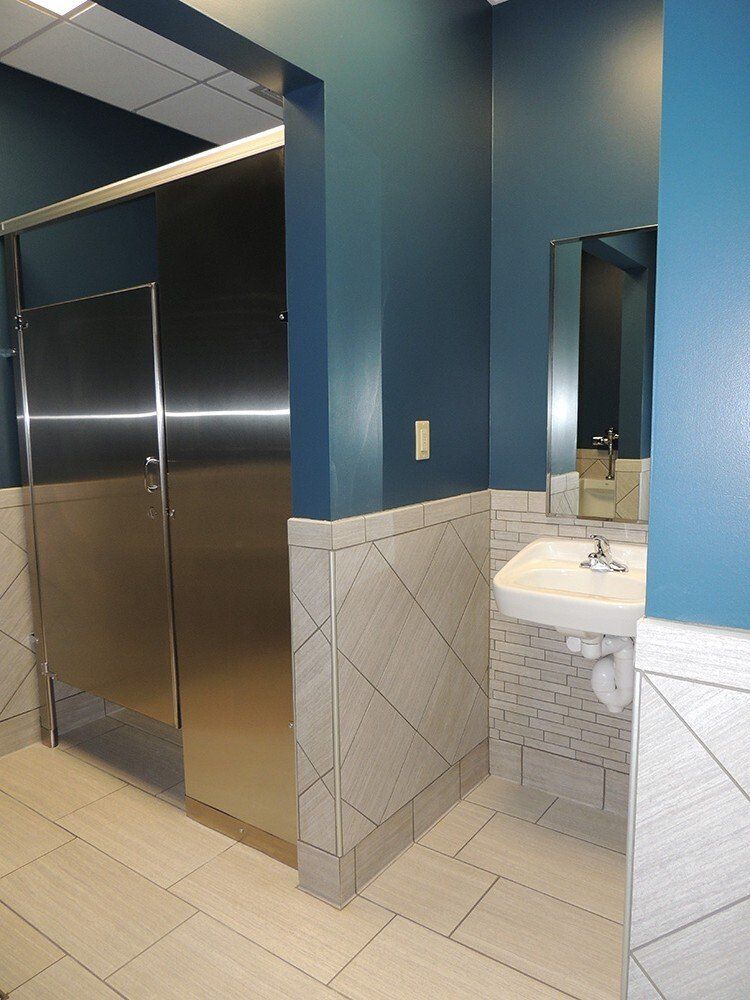 A bathroom with stainless steel stalls and a sink