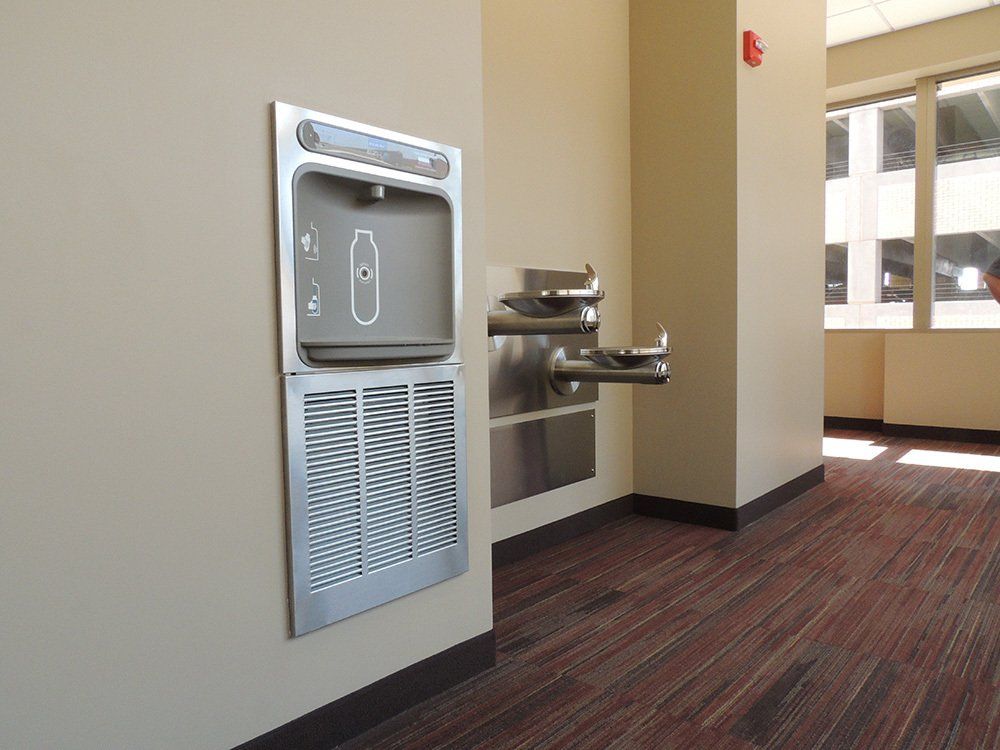 A stainless steel water fountain is mounted on a wall in a room.