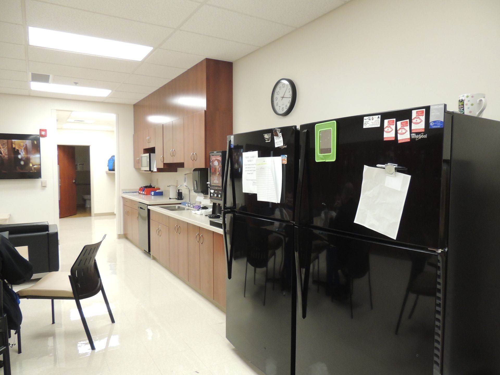 A kitchen with two black refrigerators and a clock on the wall