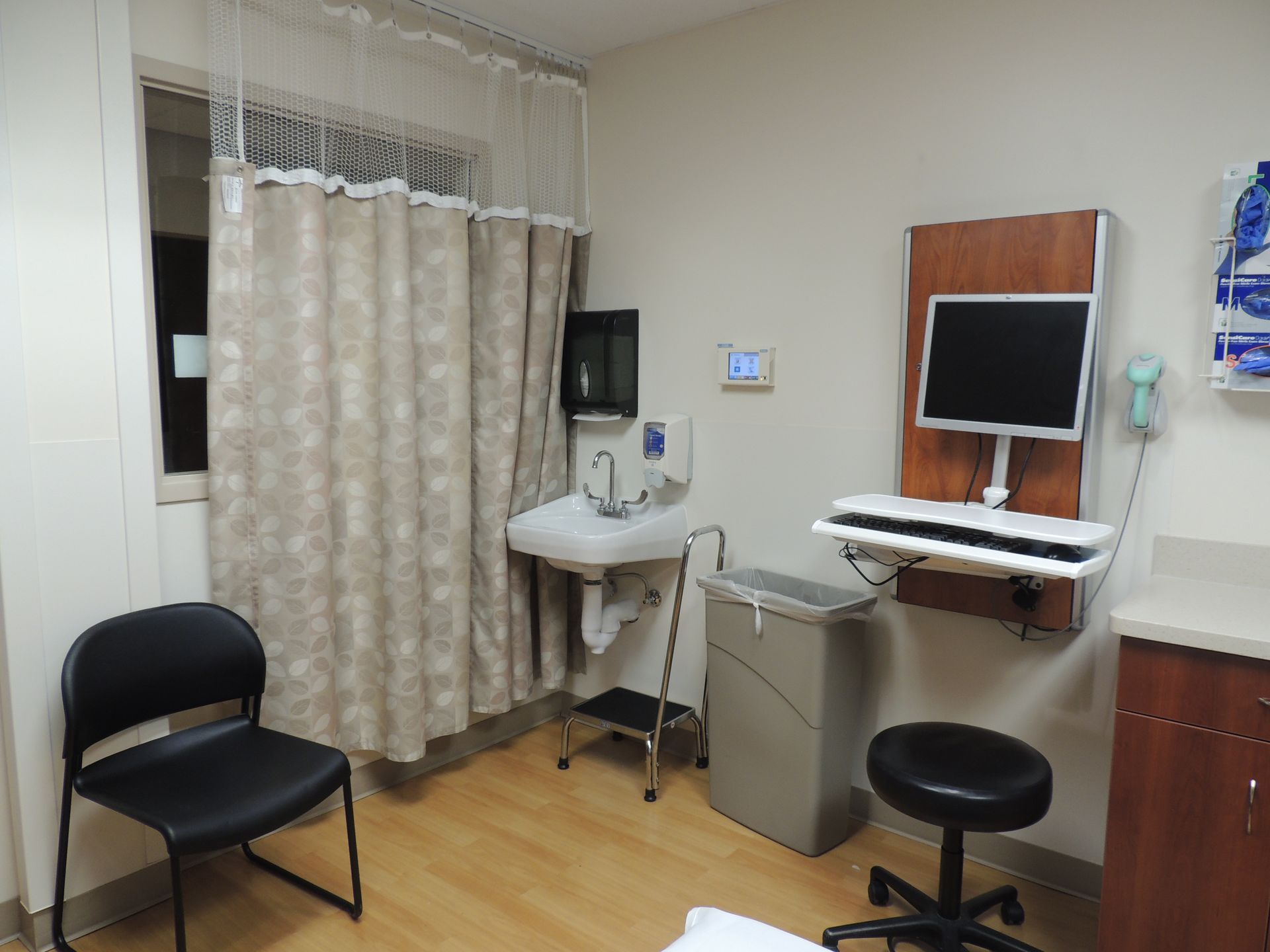 A hospital room with a sink , chairs , and a computer.