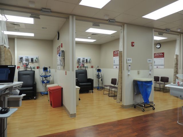 A hospital room with chairs and a blue trash can