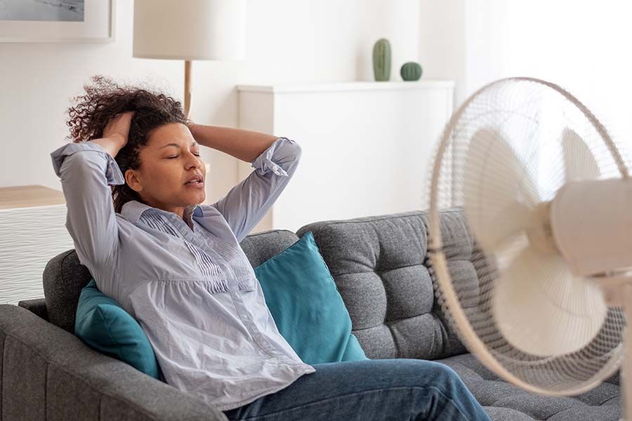 A woman is sitting on a couch in front of a fan.