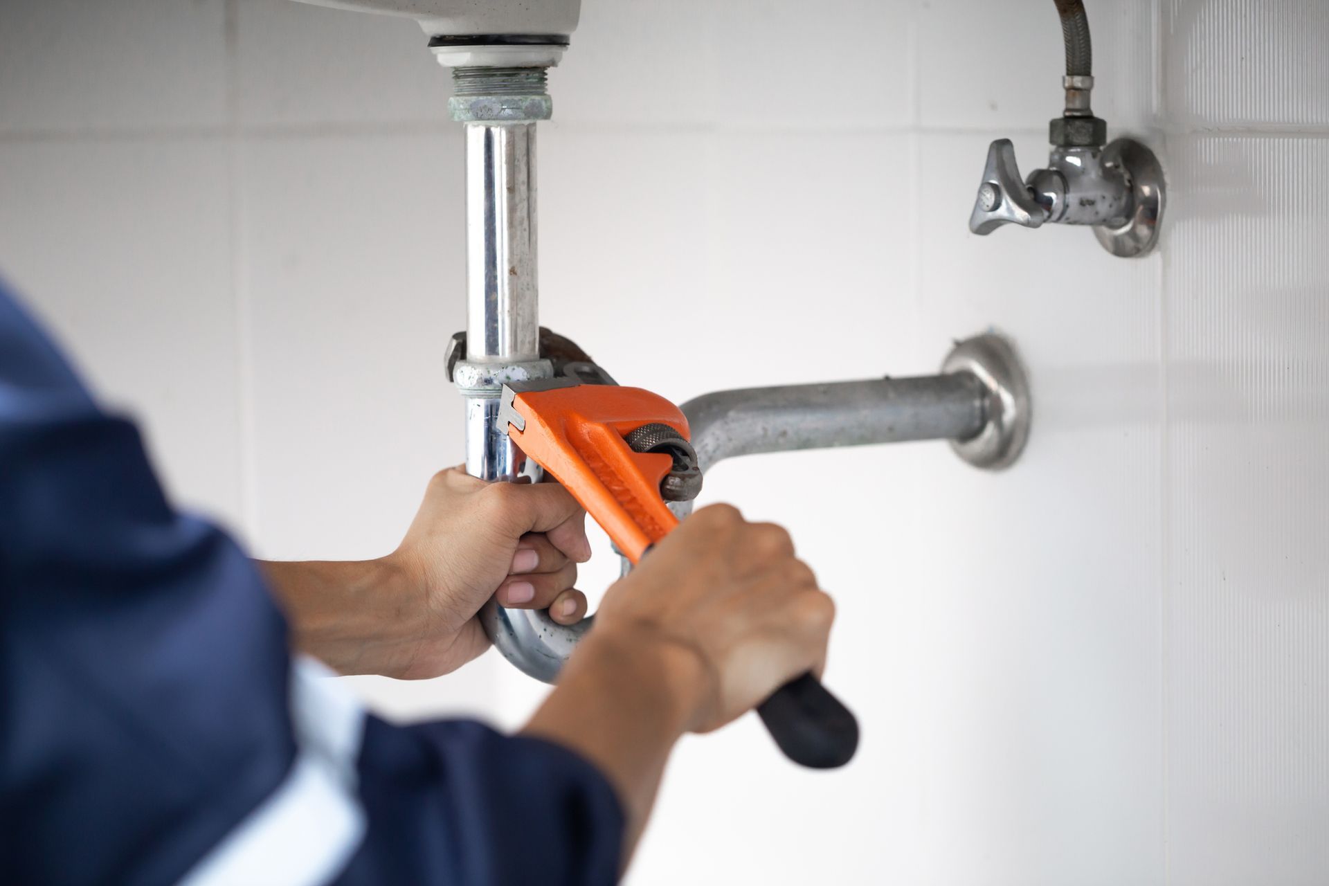 A plumber is fixing a sink pipe with a wrench.