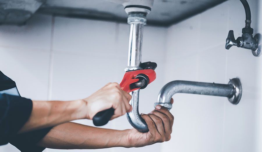 A plumber is fixing a sink pipe with a wrench.