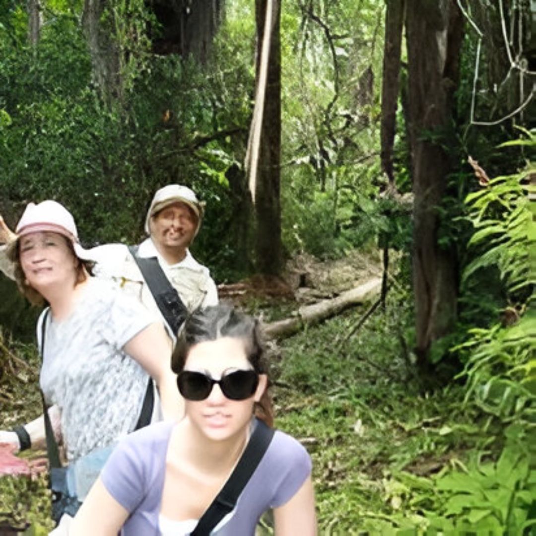 Tres personas caminando por un frondoso bosque: dos mujeres y un hombre, todos sonriendo.