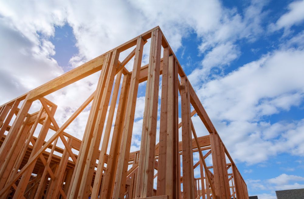 Wooden frame of a house under construction against a blue sky with clouds.