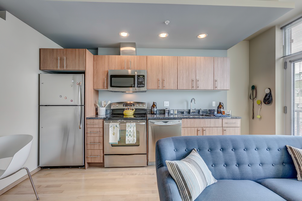 A living room with a blue couch and a kitchen with stainless steel appliances