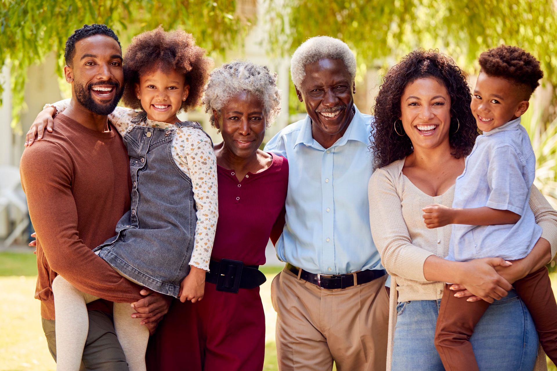 Family of six, smiling, standing in a garden, with children held in arms.