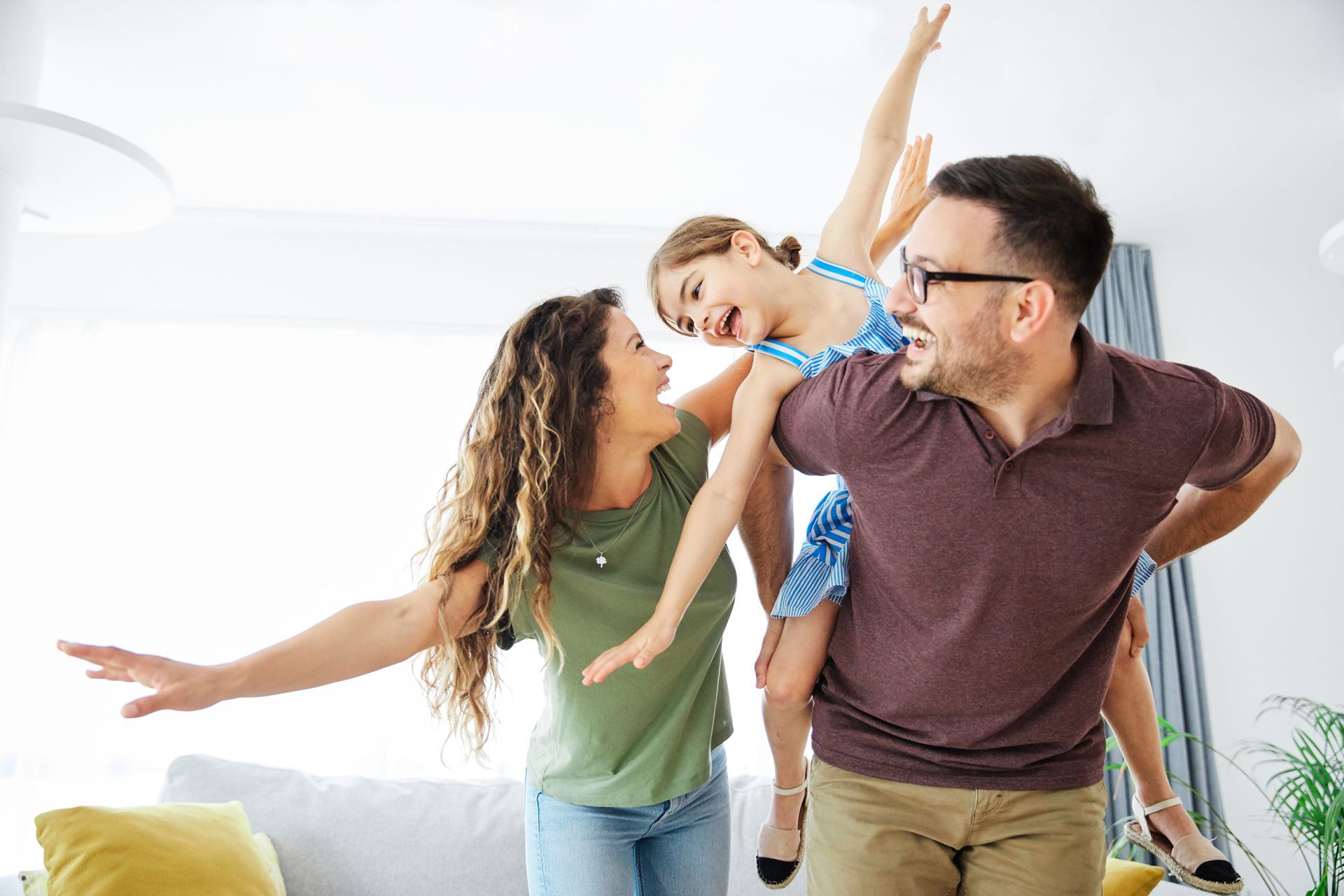 Family dancing playfully in a bright living room, with a child between two smiling adults.