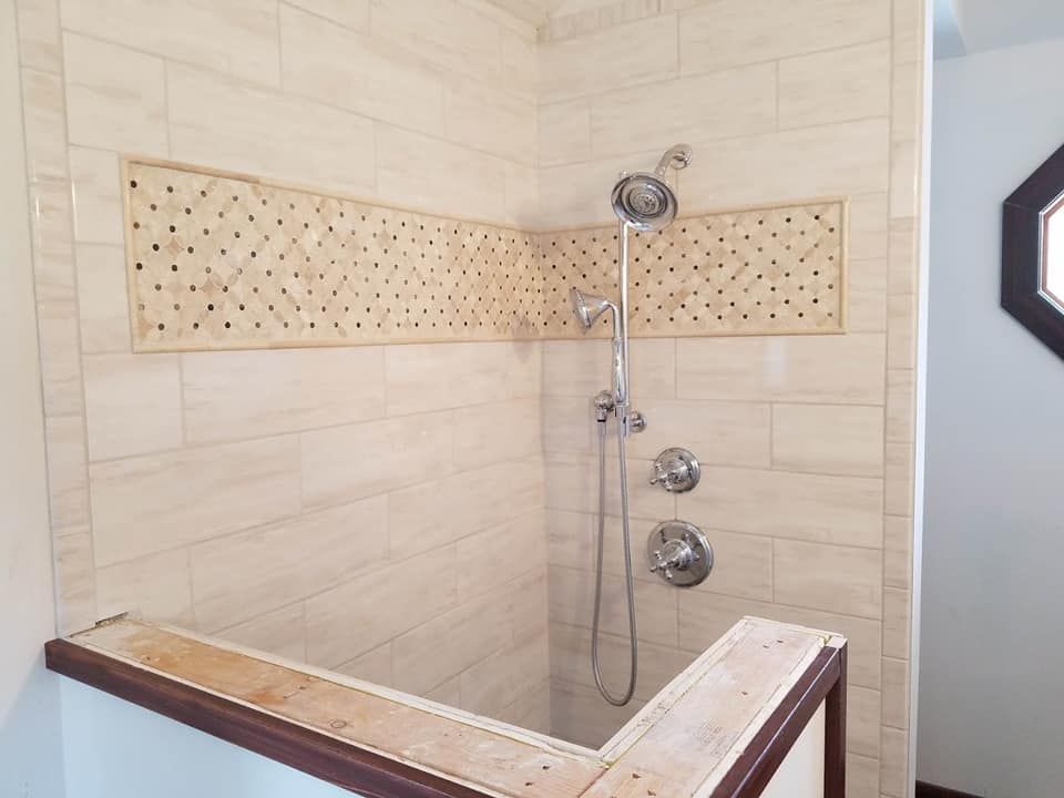 Walk-in shower with beige tile, built-in bench, decorative accent strip, and chrome shower fixtures
