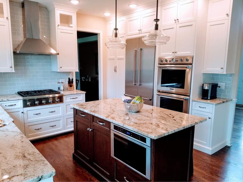 Bright white kitchen with granite island, stainless appliances, and dark wood flooring.