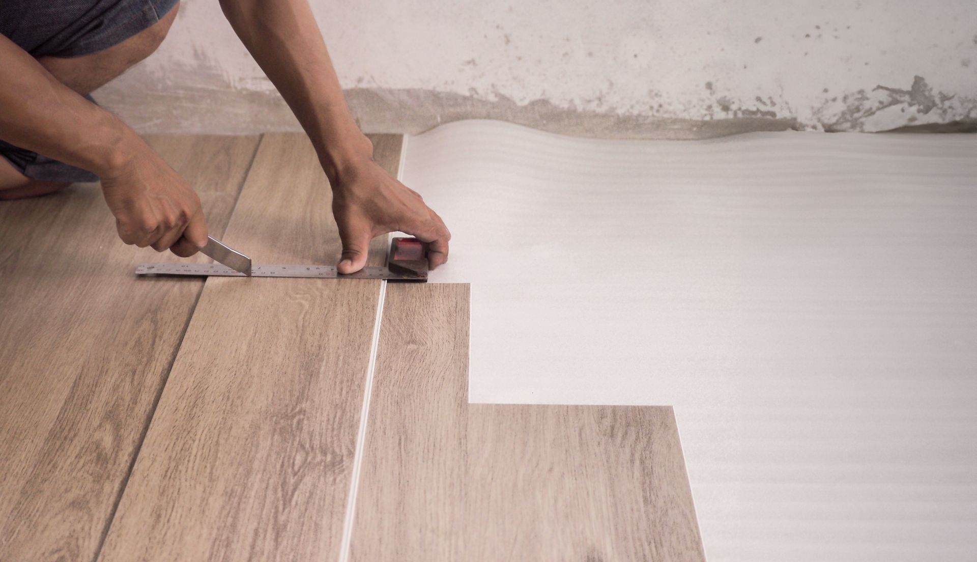 A person is cutting a piece of vinyl flooring with a pair of scissors.