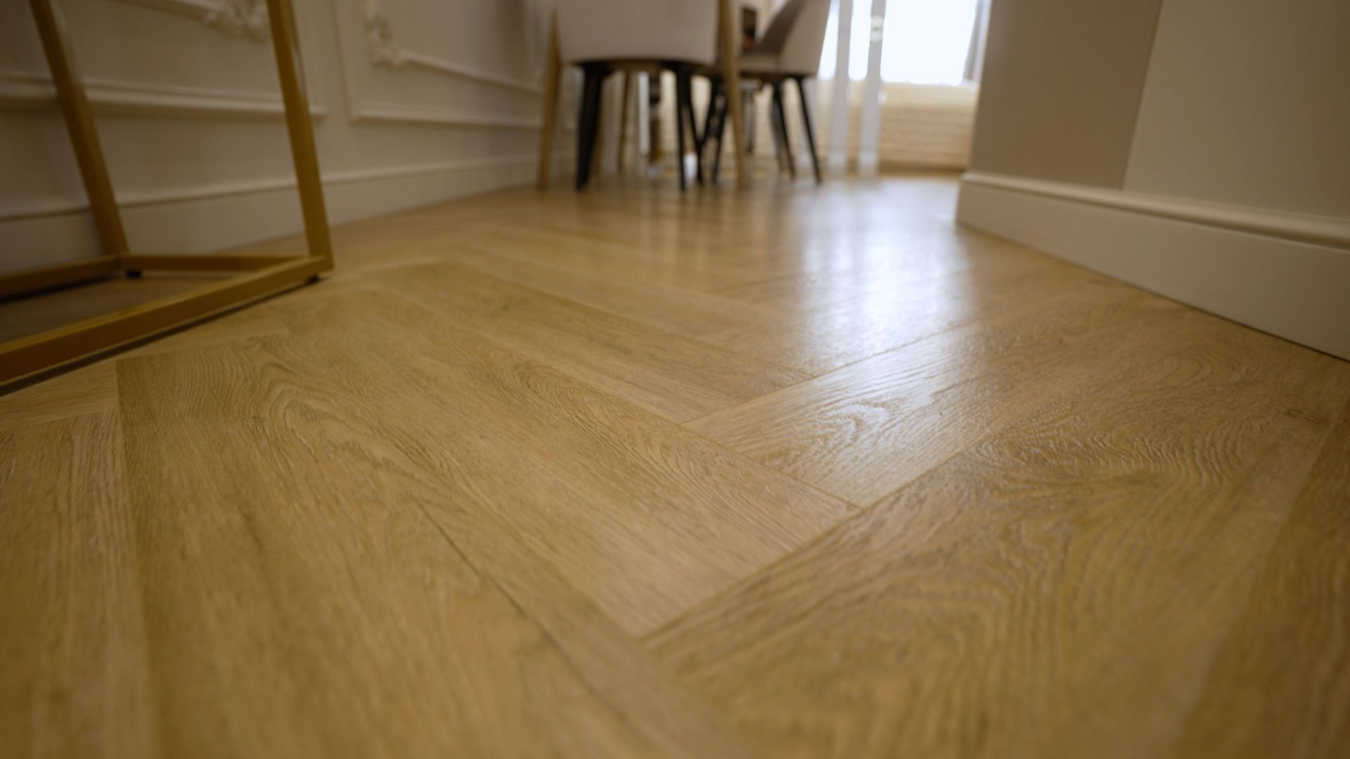 A wooden floor with a herringbone pattern in a room with a table and chairs.