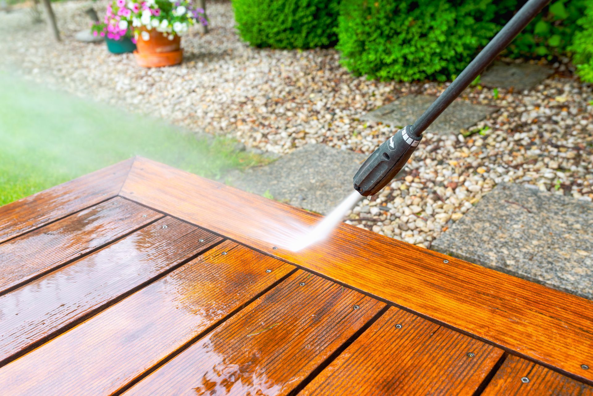 Pressure washer spraying water on a wooden deck, removing dirt.