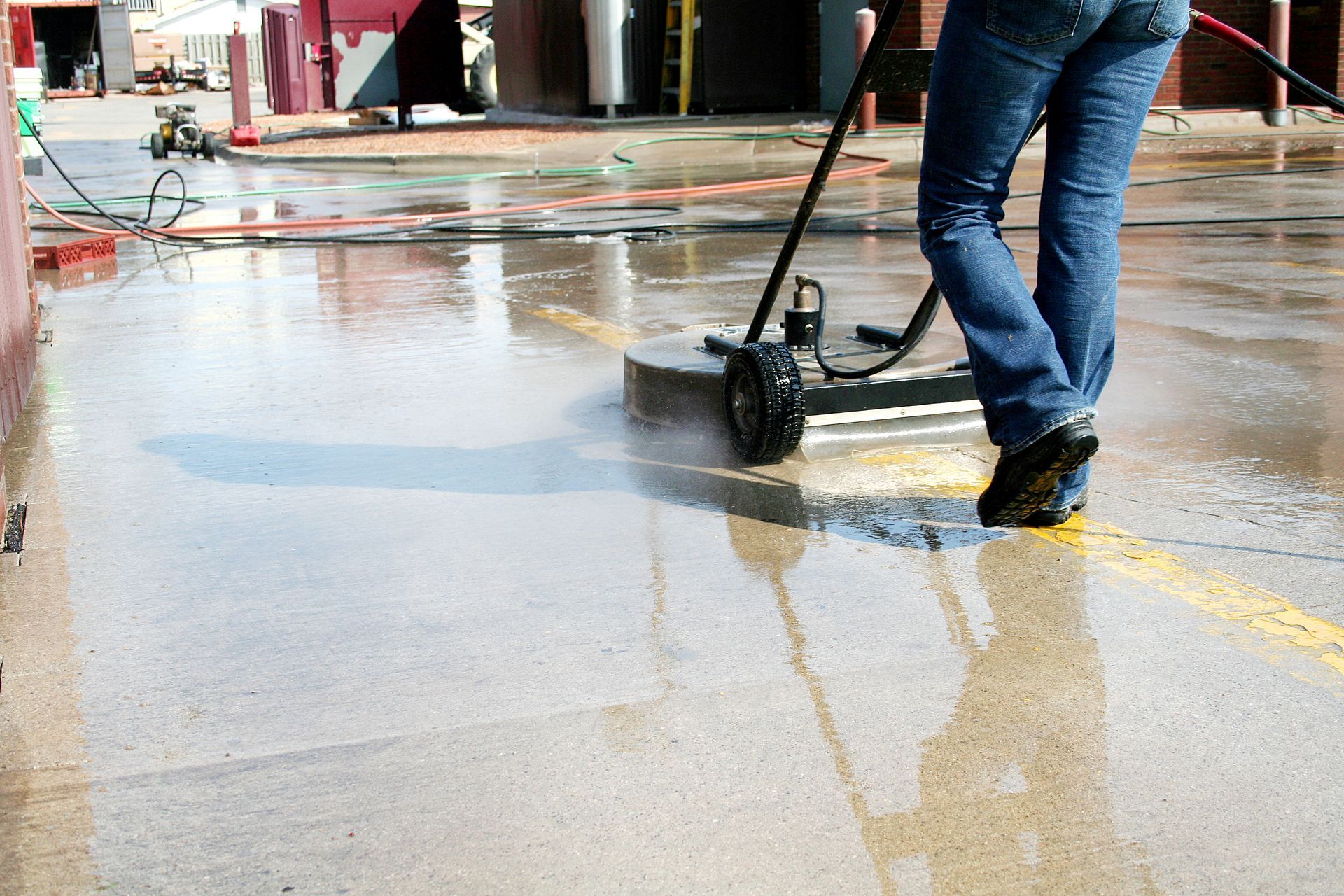 Person cleaning a wet concrete surface with a pressure washer in a parking lot.