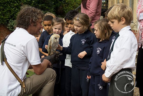 A man is holding an owl in front of a group of children.