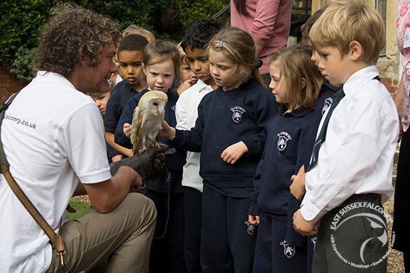 a man is holding an owl in front of a group of children .