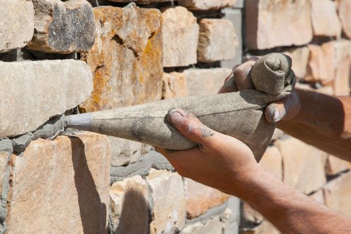 Hands holding a mortar and trowel against a stone wall, applying masonry between rocks