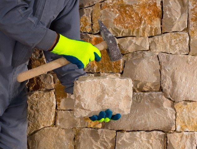 Worker in neon gloves hammering a stone wall during masonry repair