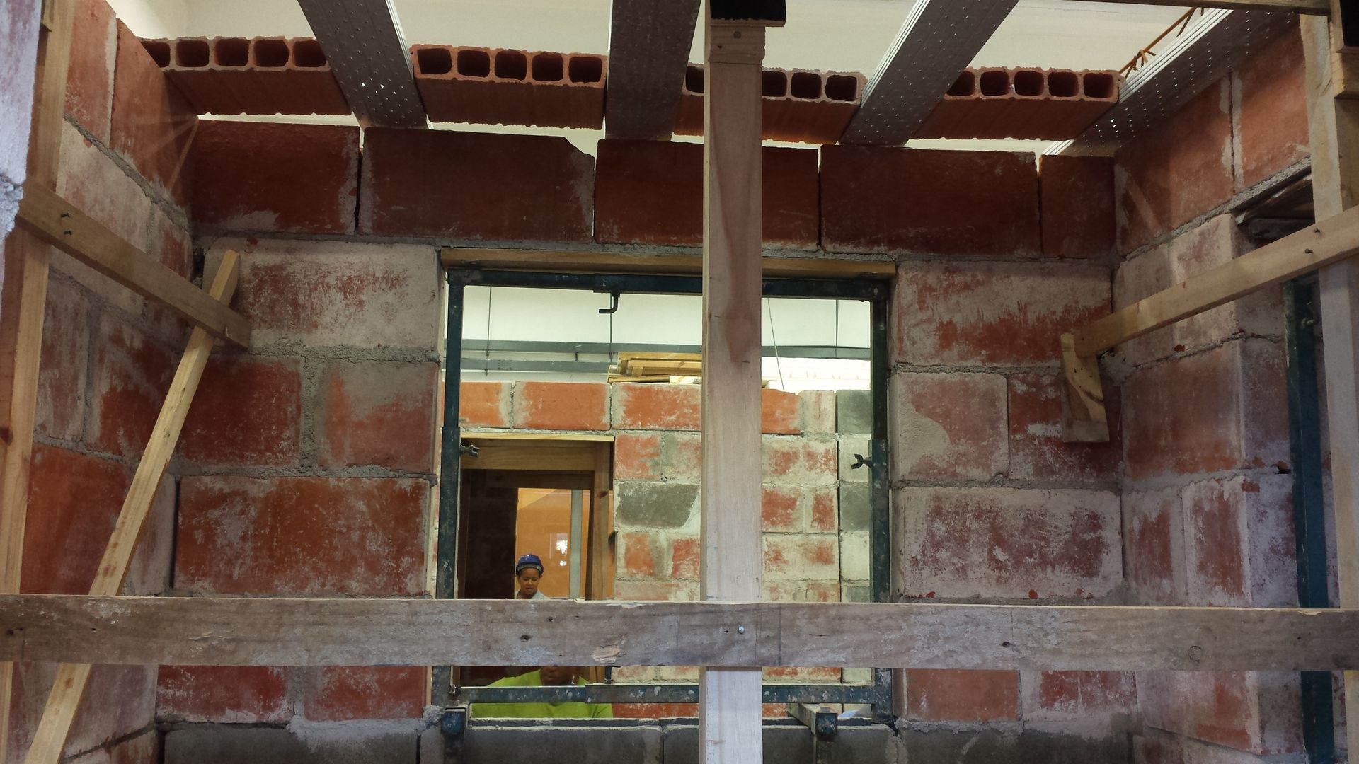 Interior of an unfinished brick building with exposed beams and a window opening into another room.