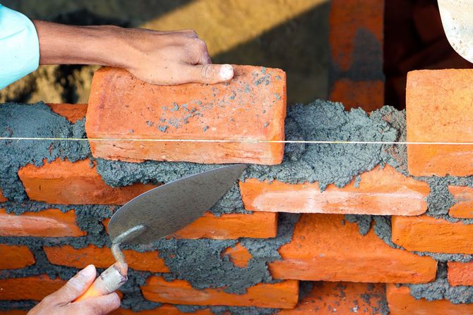 Hands laying orange bricks with mortar using a trowel on a wall