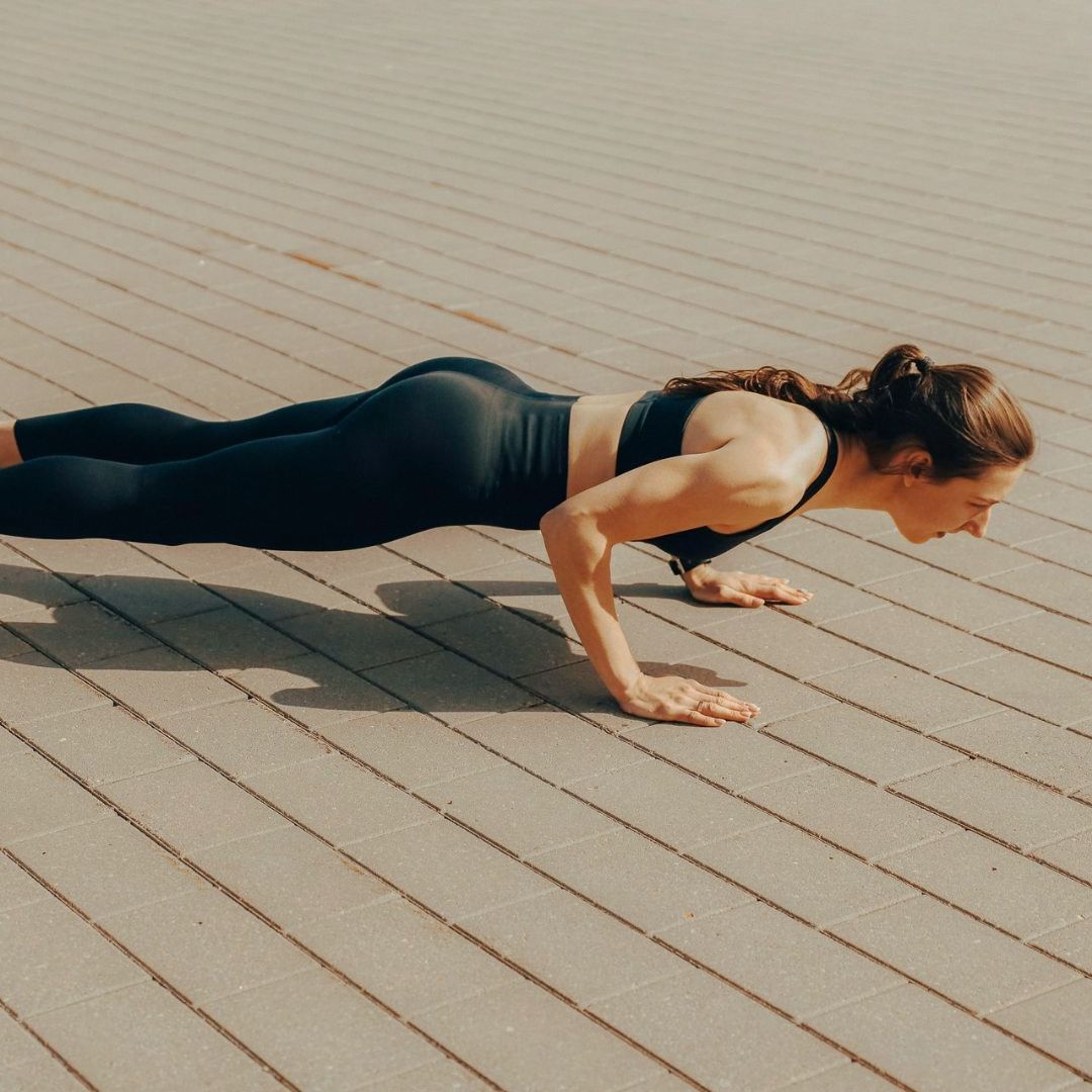 Frau in Trainingskleidung macht Liegestütze auf einer Holzoberfläche.
