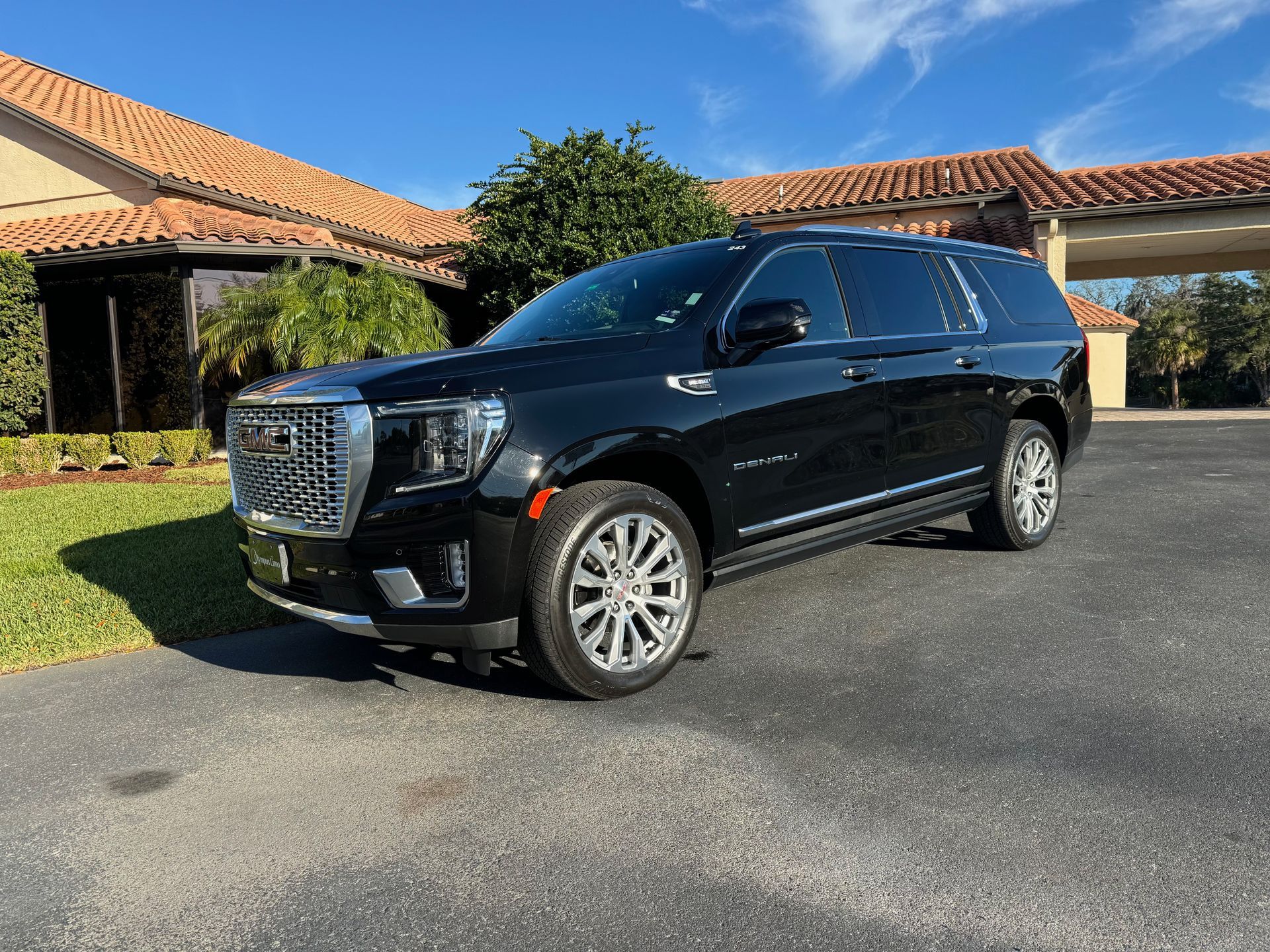Black GMC Yukon SUV parked in front of a building with a tiled roof under a blue sky.