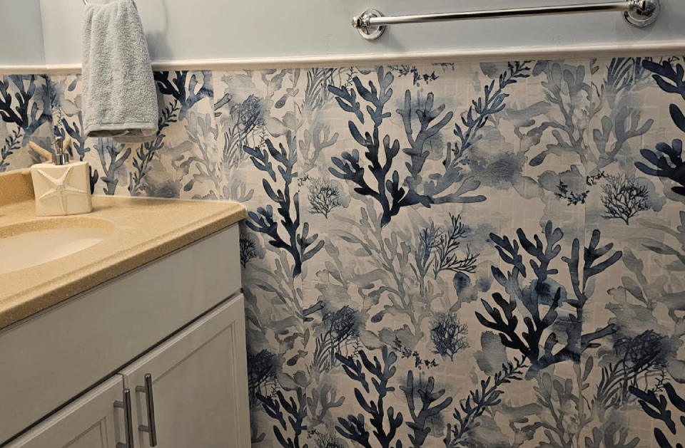 Bathroom with blue and white coral print wallpaper. Sink and vanity on the left. Towel bar with towel.