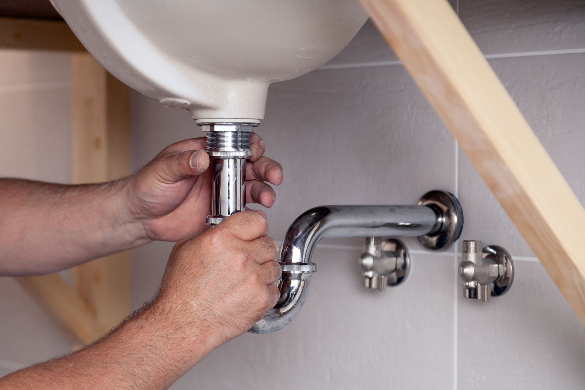 Hands assembling sink plumbing pipes under a white ceramic sink.