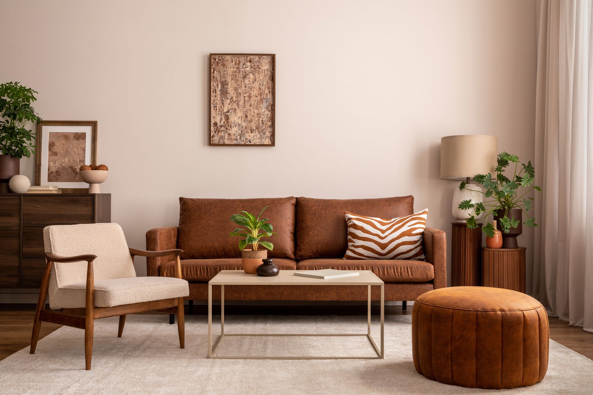 Living room with brown leather sofa, wooden chair, plants, and rug.