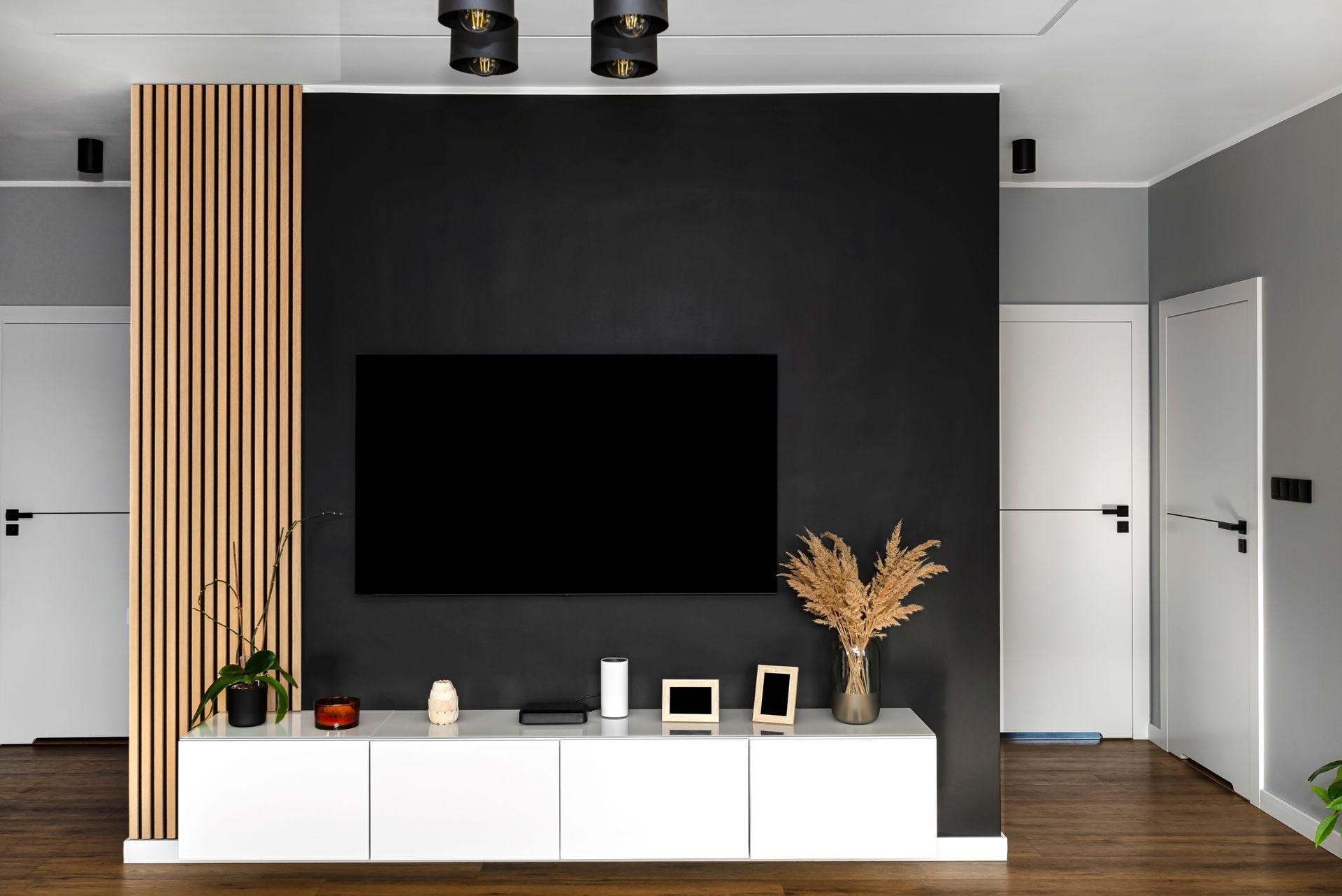 Black accent wall with mounted TV, white console, and wooden slat detail; two white doors.