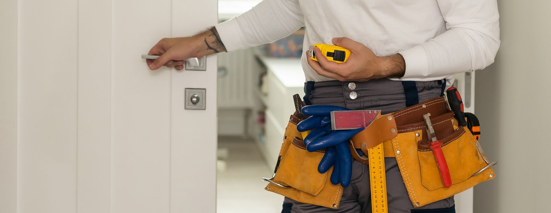 A person in a tool belt holding a measuring tape and opening a door.