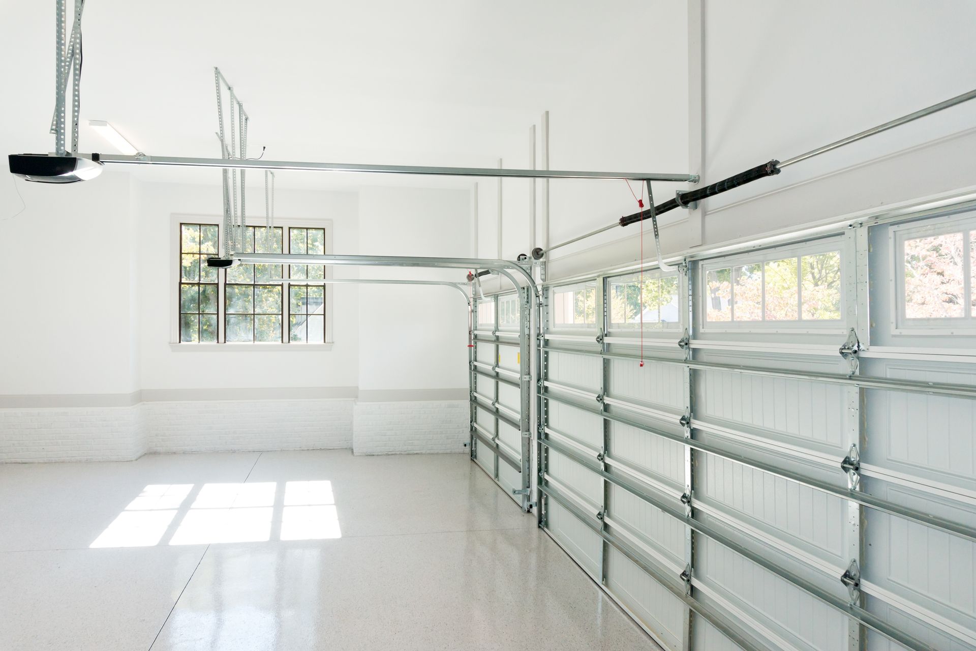 Empty, bright white garage interior with overhead door, window, and glossy floor.
