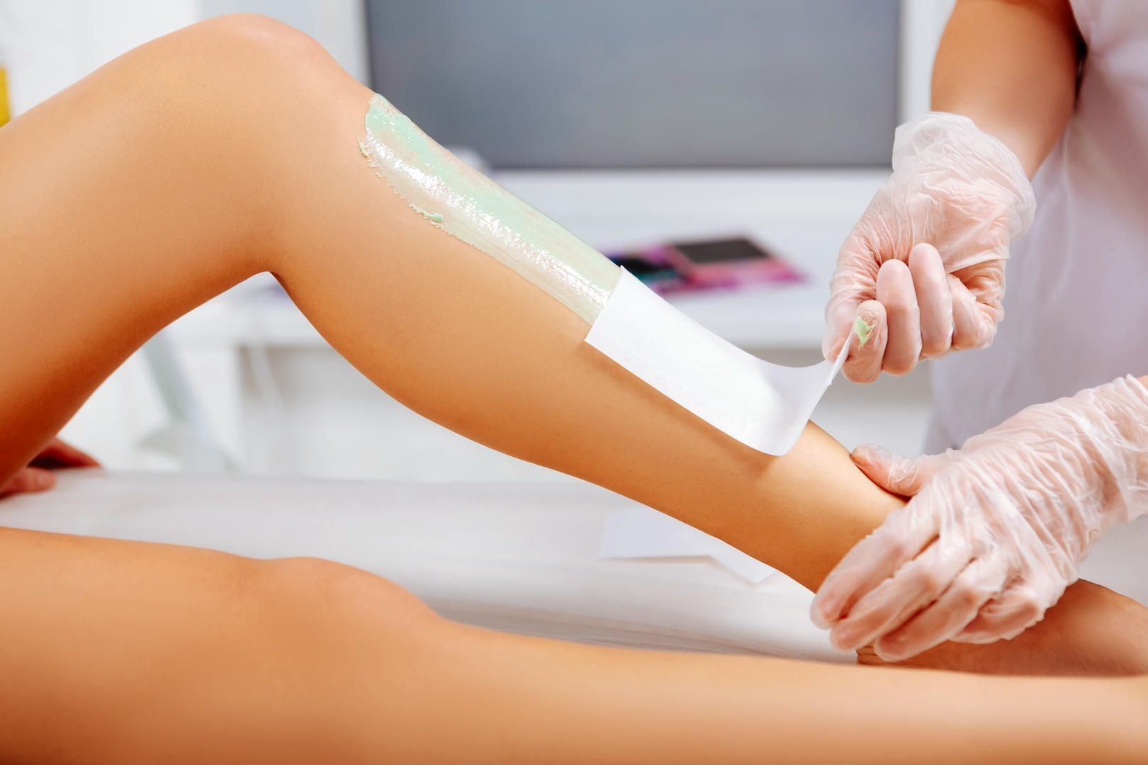 Leg being waxed at a salon. A beautician peels off a wax strip.